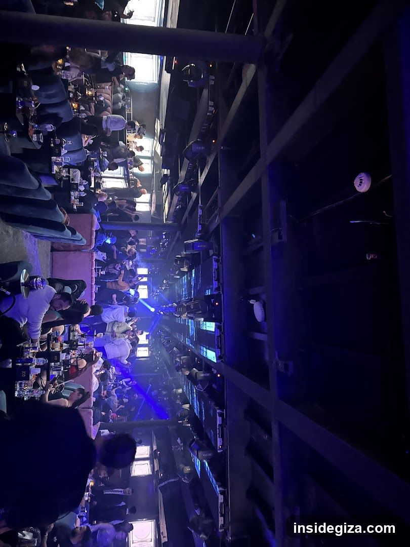 A crowded indoor venue with blue lighting, featuring a stage area and multiple seating sections filled with people.