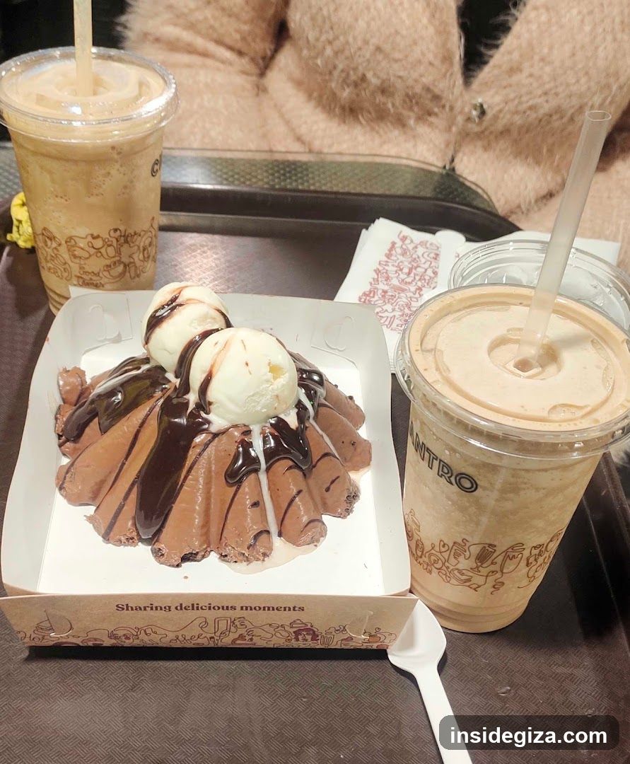 A tray featuring a chocolate ice cream dessert topped with two scoops of vanilla ice cream and drizzled with chocolate sauce, accompanied by two cups of iced coffee. The setting appears to be indoors, likely in a café or dessert shop.